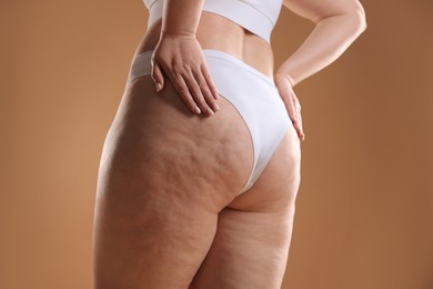 Woman with cellulite on light brown background, closeup