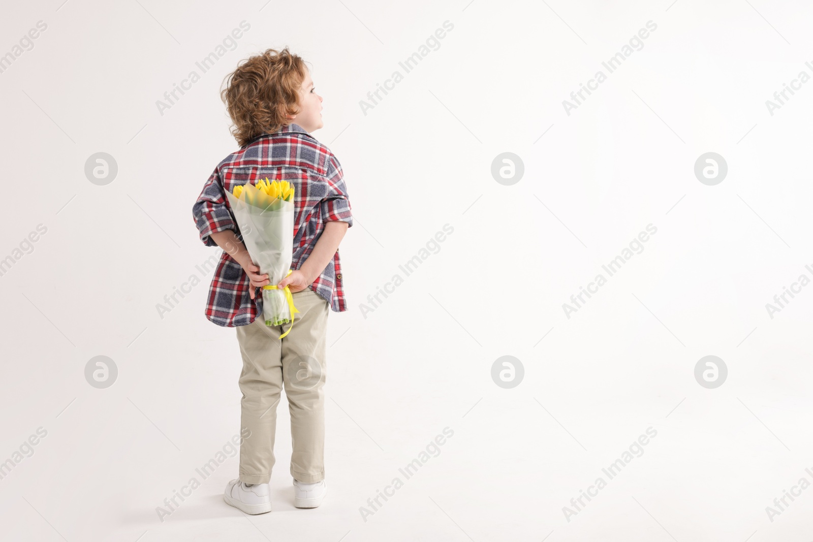 Photo of Little boy with bouquet of tulips behind his back on white background. Space for text