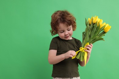 Photo of Cute little boy with bouquet of tulips on green background