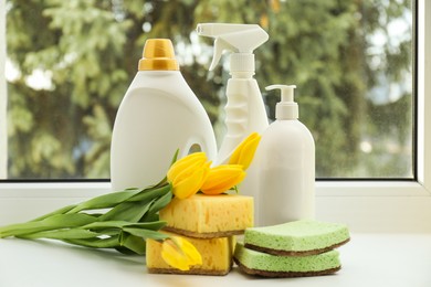 Photo of Spring cleaning. Detergents, supplies and tulips on windowsill indoors