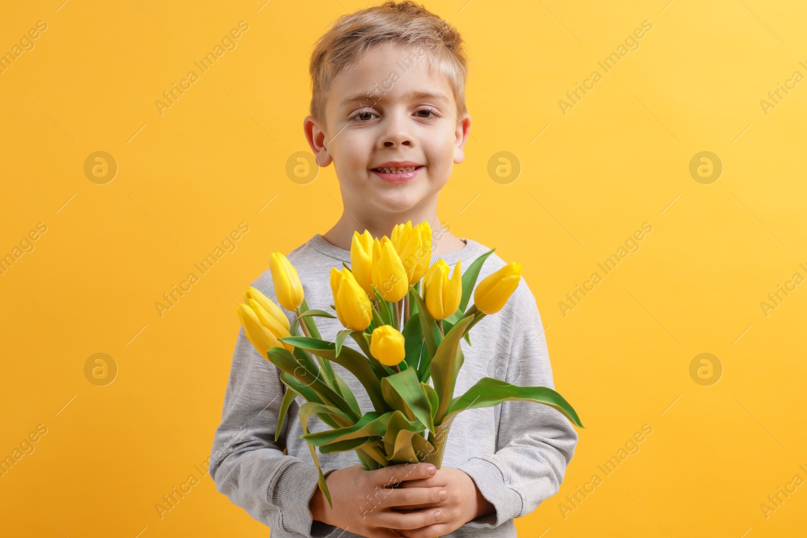 Photo of Cute little boy with bouquet of tulips on yellow background