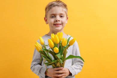 Cute little boy with bouquet of tulips on yellow background