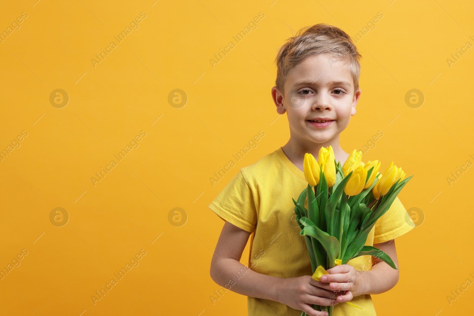 Photo of Cute little boy with bouquet of tulips on yellow background. Space for text