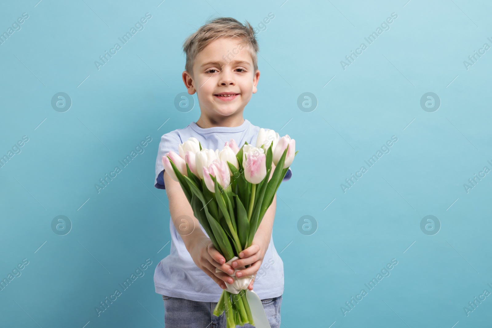 Photo of Cute little boy with bouquet of tulips on light blue background