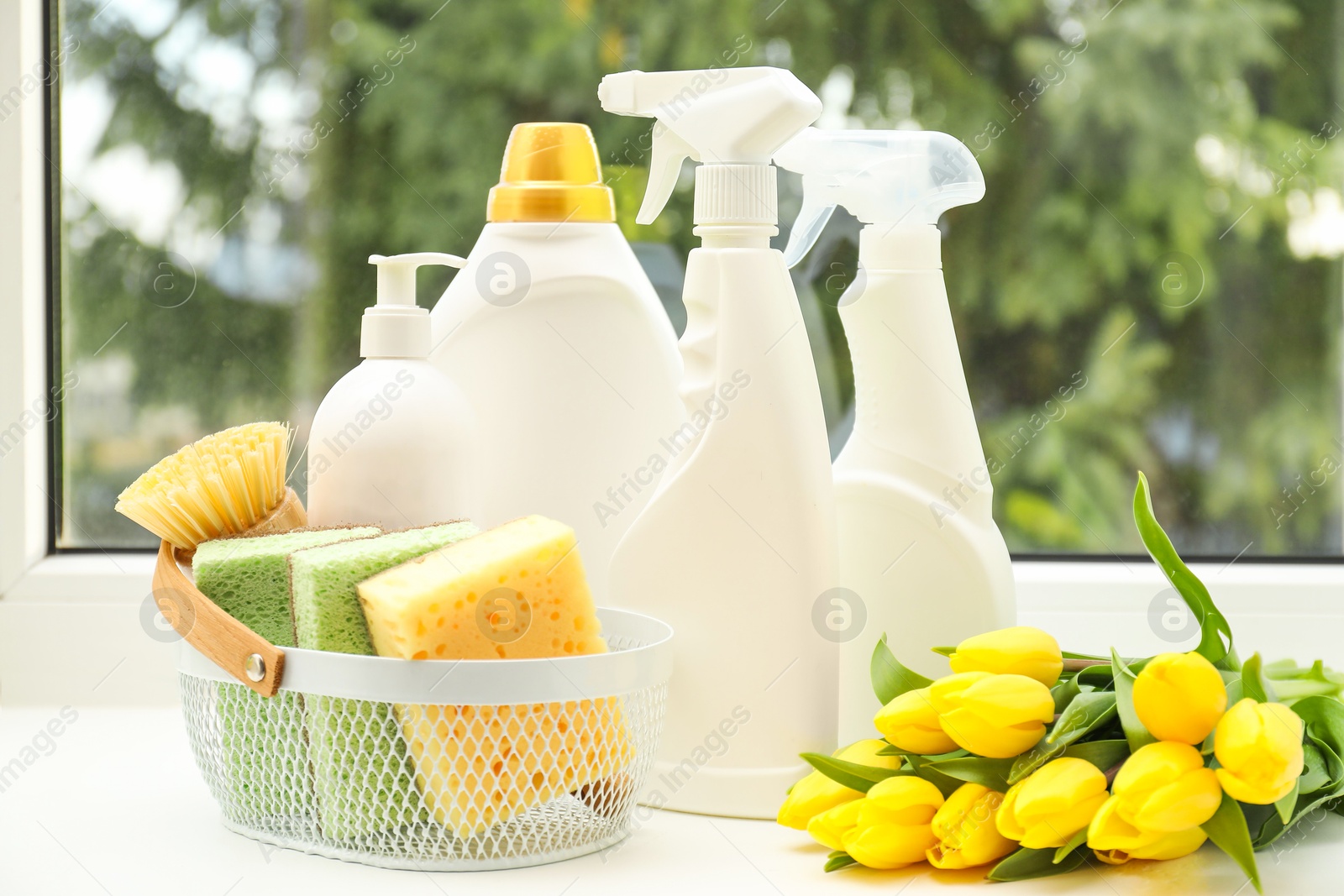 Photo of Spring cleaning. Detergents, supplies and tulips on windowsill indoors