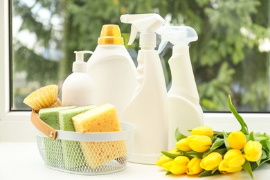 Photo of Spring cleaning. Detergents, supplies and tulips on windowsill indoors