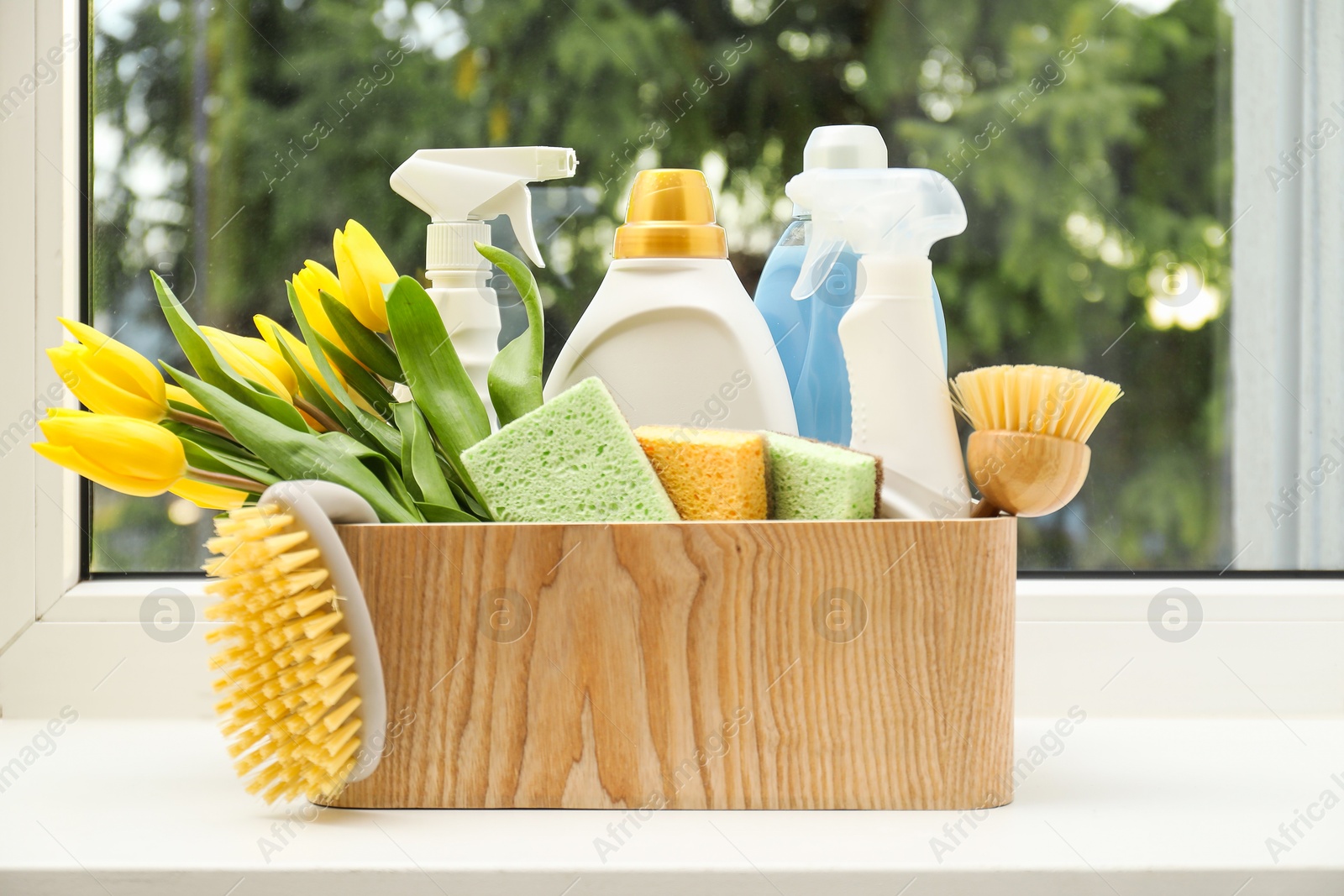 Photo of Spring cleaning. Detergents, supplies and tulips on windowsill indoors