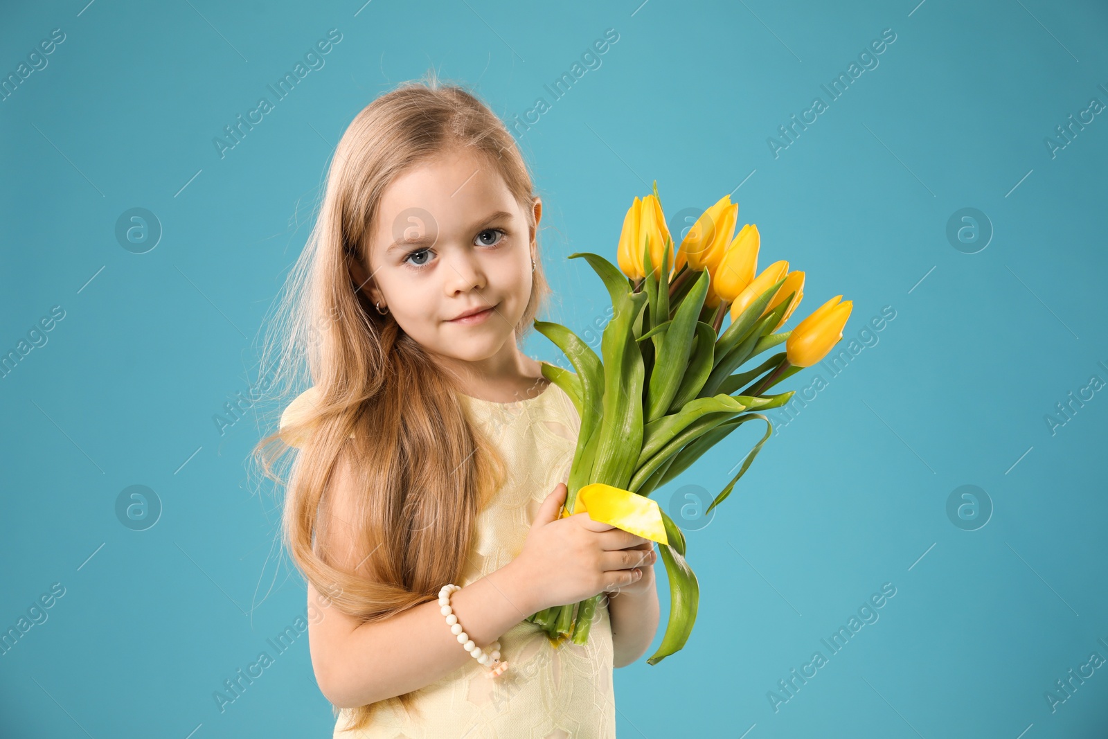 Photo of Cute little girl with beautiful yellow tulips on light blue background. Spring season