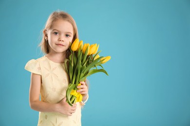 Photo of Cute little girl with beautiful yellow tulips on light blue background, space for text. Spring season