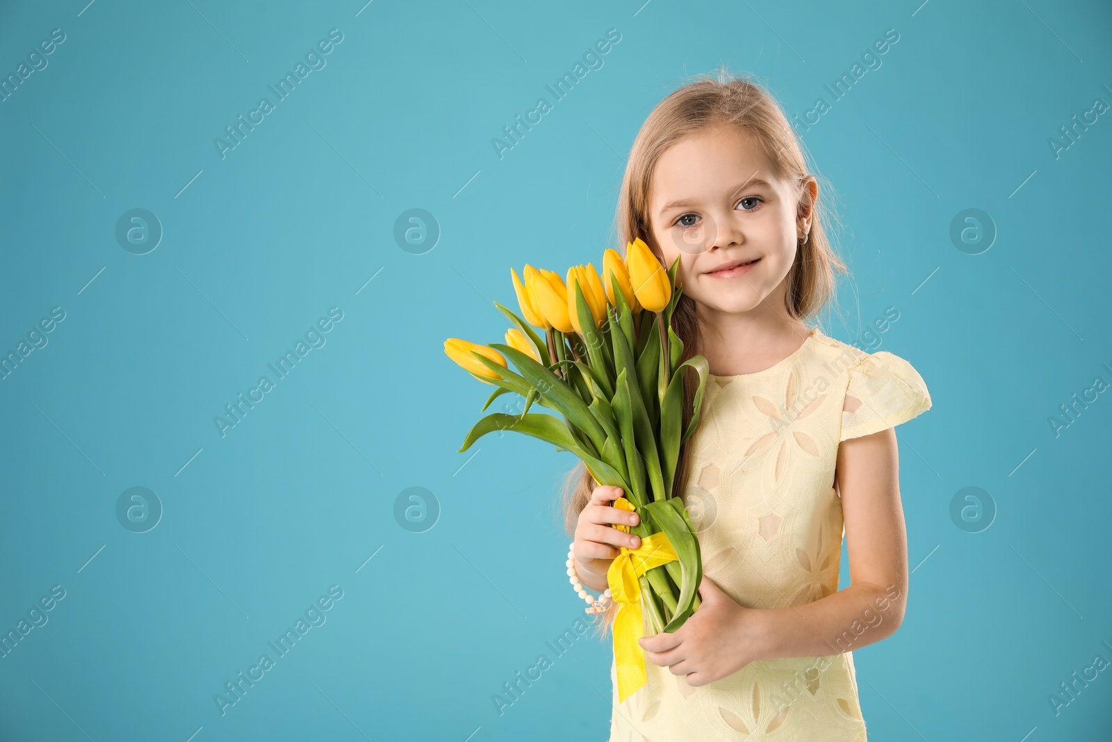 Photo of Cute little girl with beautiful yellow tulips on light blue background, space for text. Spring season