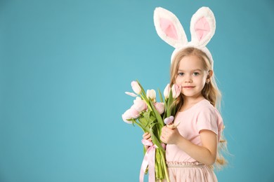 Photo of Cute little girl with bunny ears and spring flowers on light blue background, space for text. Easter celebration