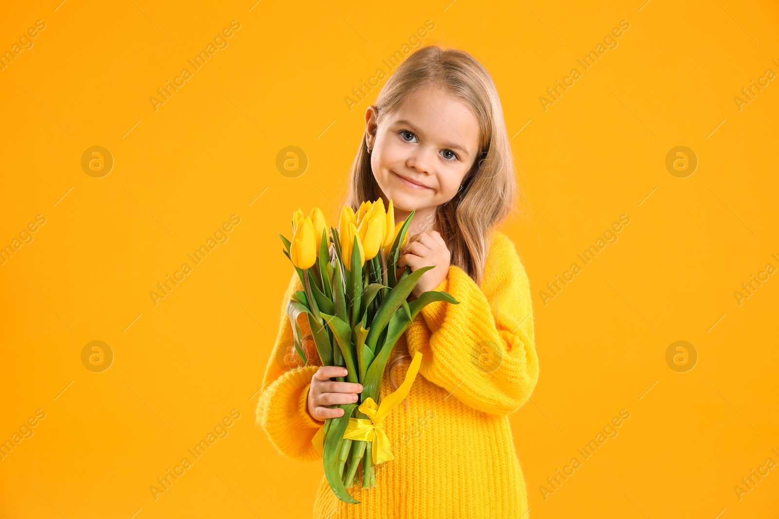 Photo of Cute little girl with beautiful yellow tulips on orange background. Spring season