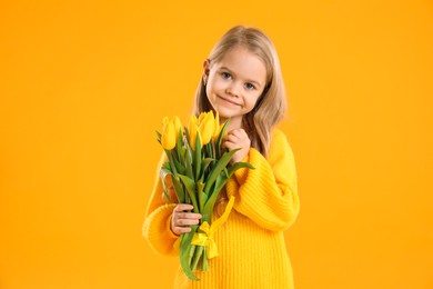 Photo of Cute little girl with beautiful yellow tulips on orange background. Spring season