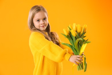 Photo of Cute little girl with beautiful yellow tulips on orange background. Spring season