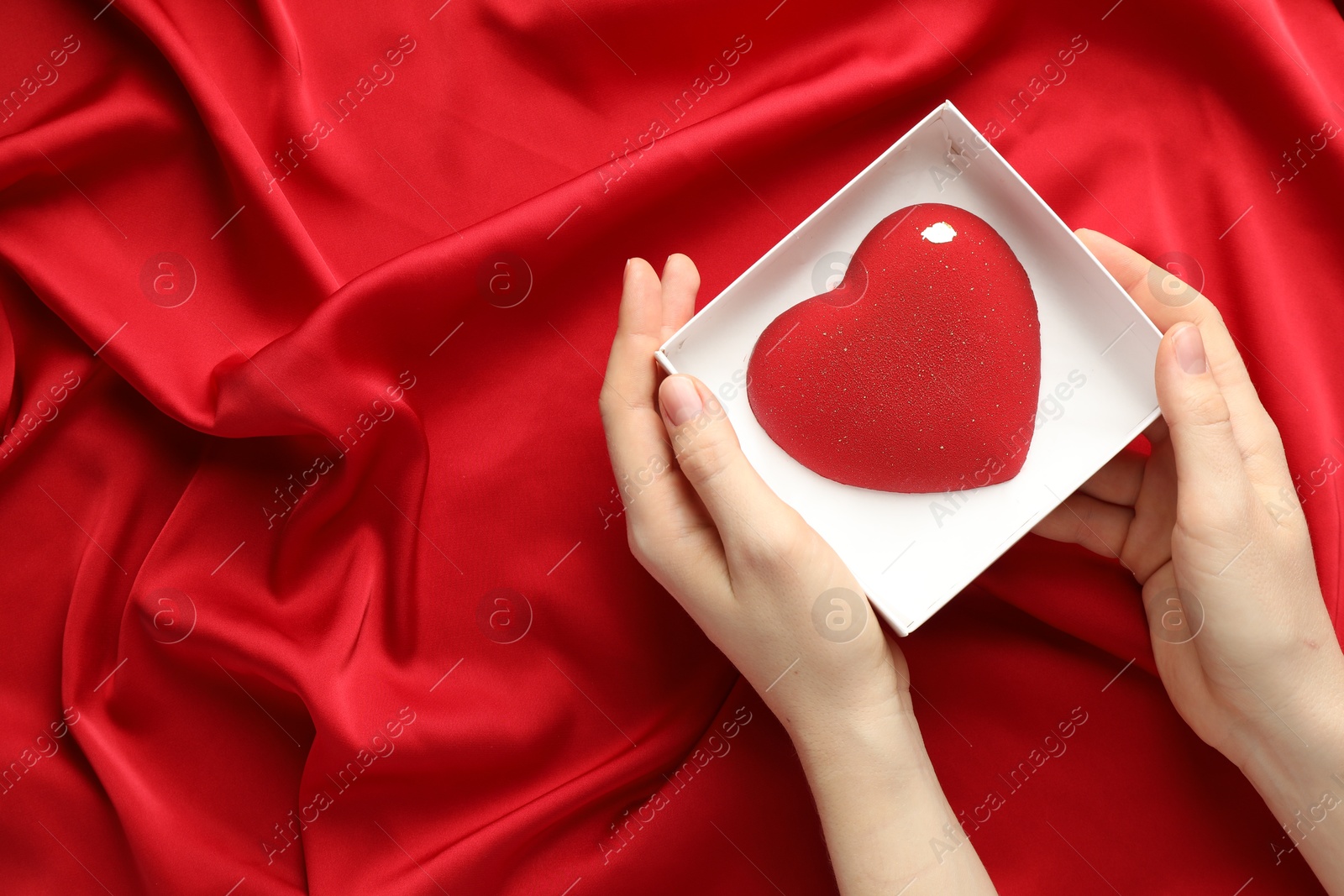 Photo of Woman with heart shaped chocolate in box on red fabric background, top view. Space for text