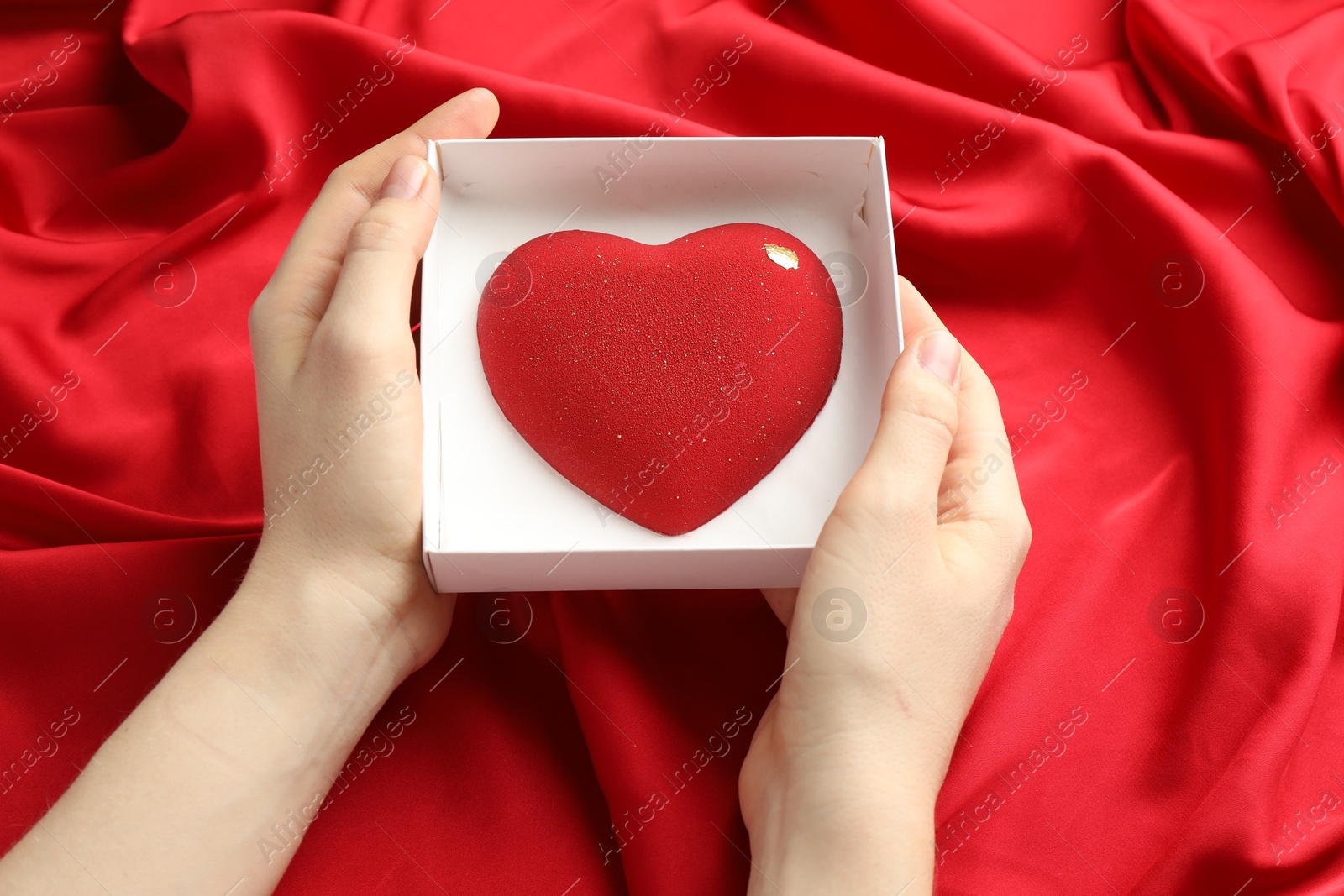 Photo of Woman with heart shaped chocolate in box on red fabric background, closeup