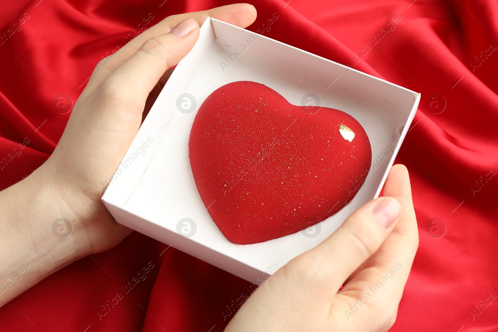 Photo of Woman with heart shaped chocolate in box on red fabric background, closeup