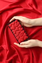 Photo of Woman holding chocolate bar decorated with hearts on red fabric background, top view