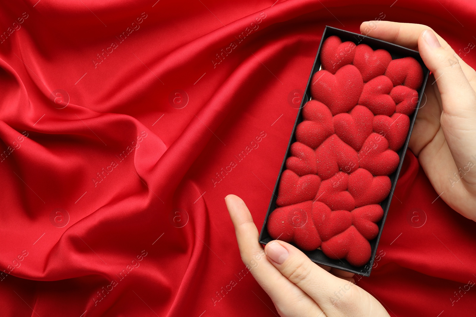 Photo of Woman holding chocolate bar decorated with hearts on red fabric background, top view. Space for text