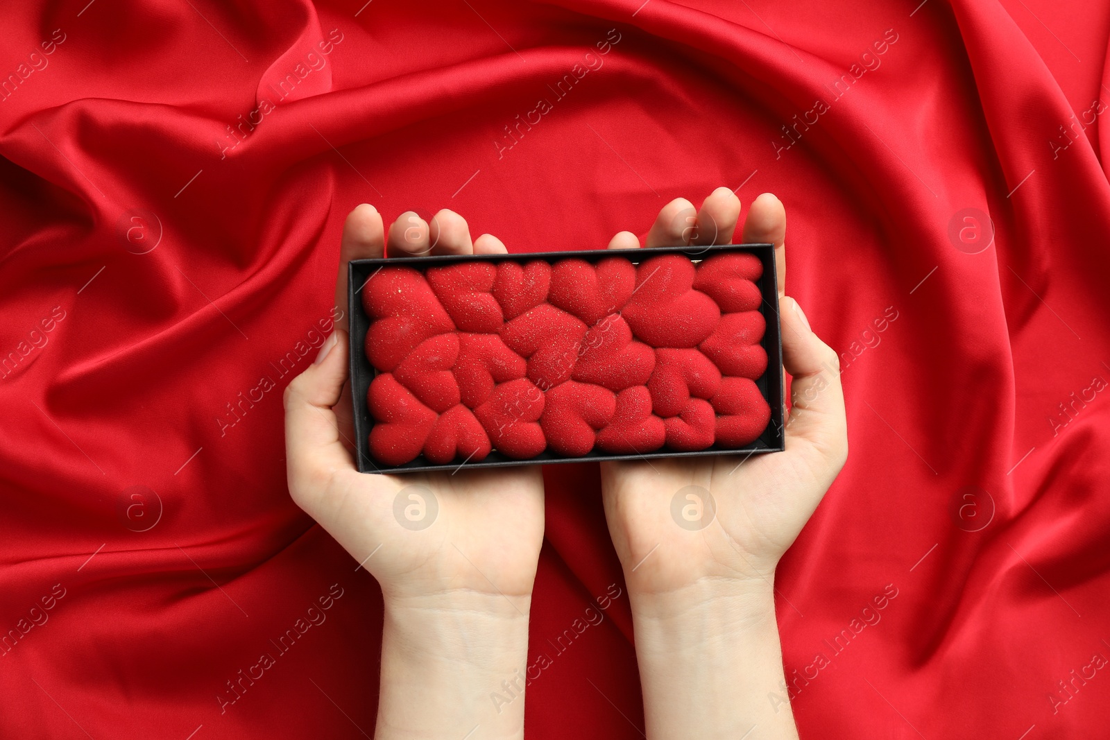 Photo of Woman holding chocolate bar decorated with hearts on red fabric background, top view