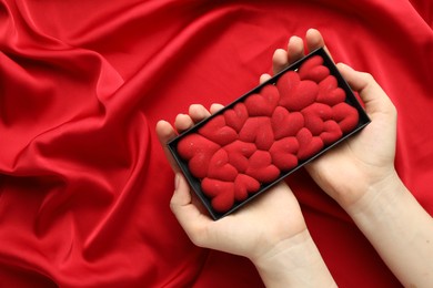 Photo of Woman holding chocolate bar decorated with hearts on red fabric background, top view. Space for text