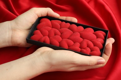 Photo of Woman holding chocolate bar decorated with hearts on red fabric background, closeup