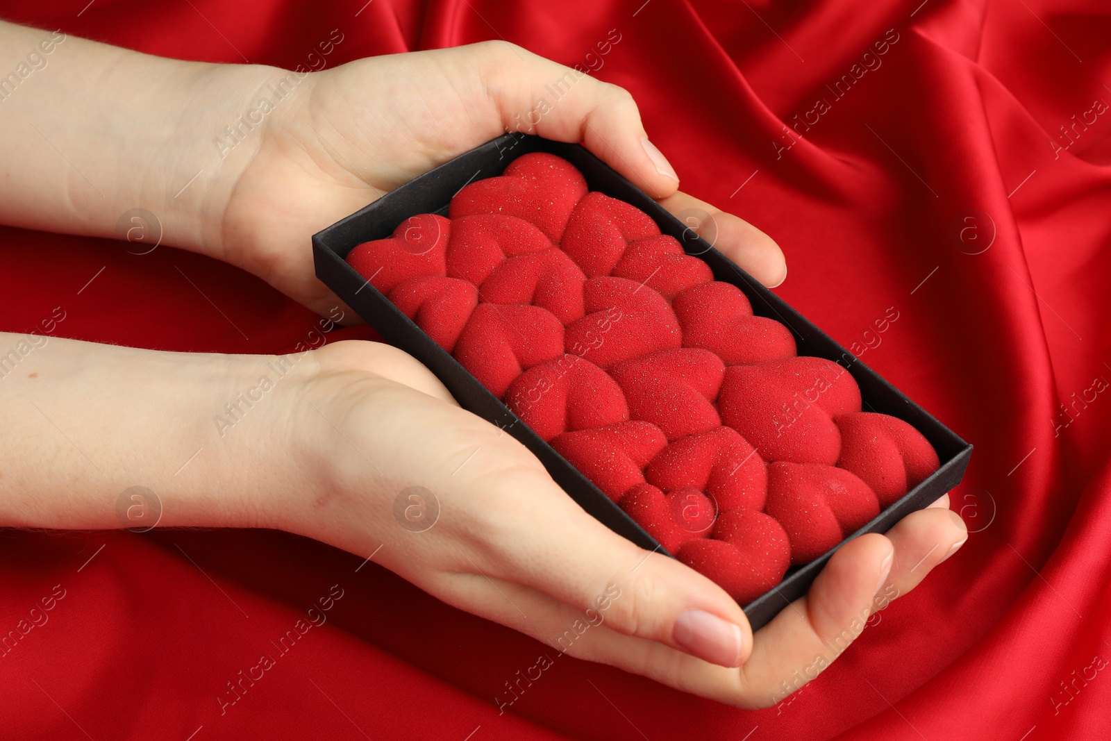 Photo of Woman holding chocolate bar decorated with hearts on red fabric background, closeup