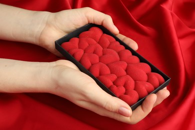 Photo of Woman holding chocolate bar decorated with hearts on red fabric background, closeup