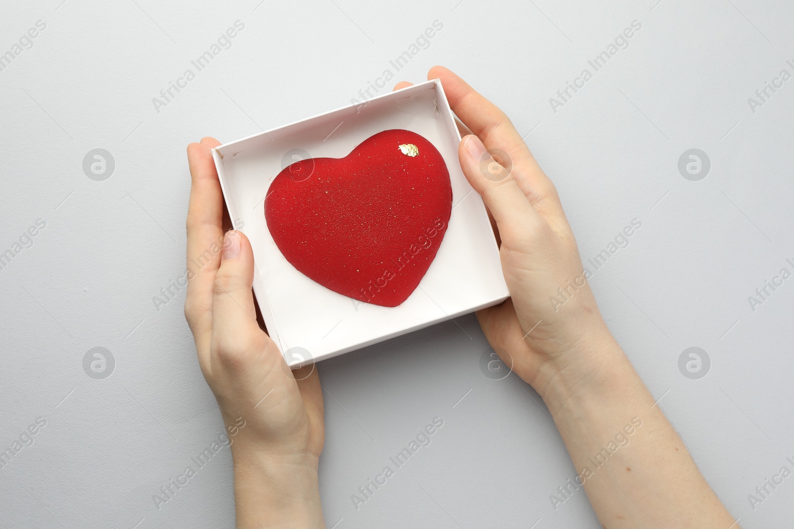 Photo of Woman with heart shaped chocolate in box on white background, top view