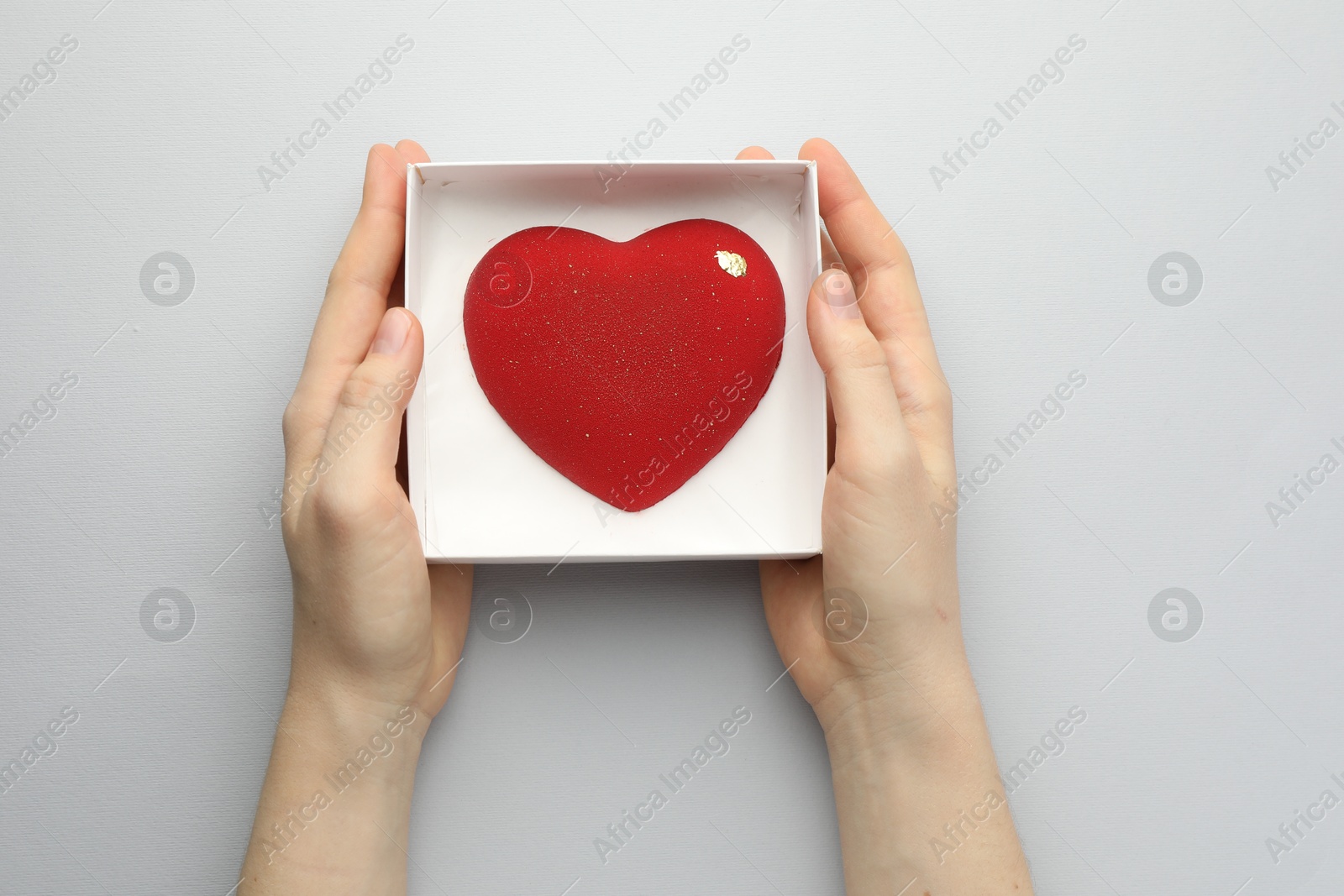 Photo of Woman with heart shaped chocolate in box on white background, top view