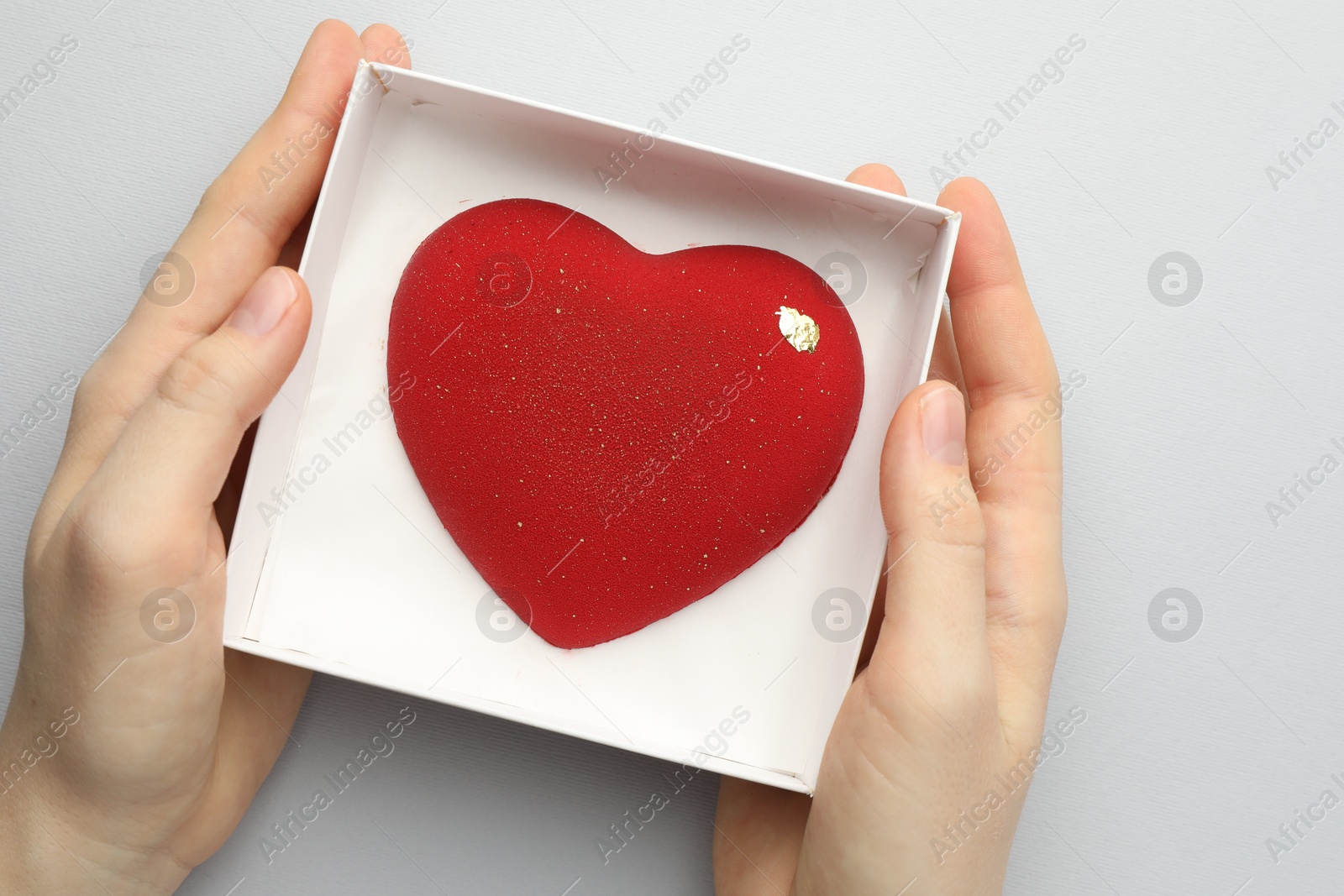 Photo of Woman with heart shaped chocolate in box on white background, top view