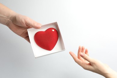 Photo of Man gifting woman heart shaped chocolate on white background, closeup. Space for text