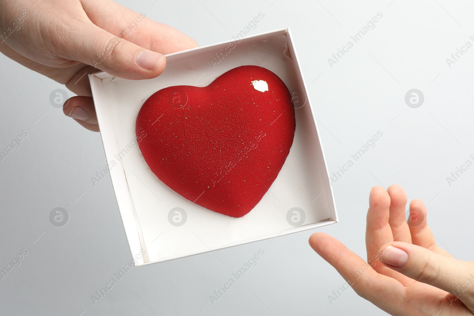 Photo of Man gifting woman heart shaped chocolate on white background, closeup