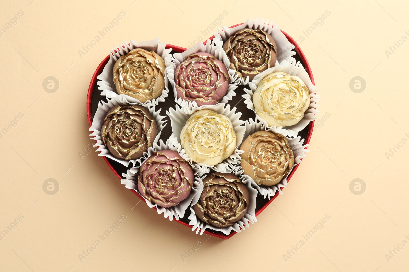 Photo of Flower shaped chocolate bonbons in box on beige background, top view