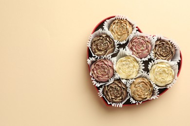 Photo of Flower shaped chocolate bonbons in box on beige background, top view. Space for text