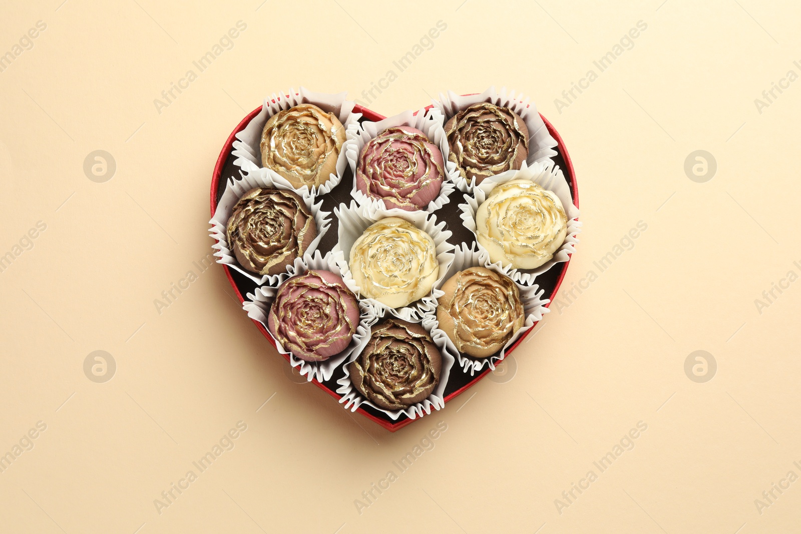 Photo of Flower shaped chocolate bonbons in box on beige background, top view