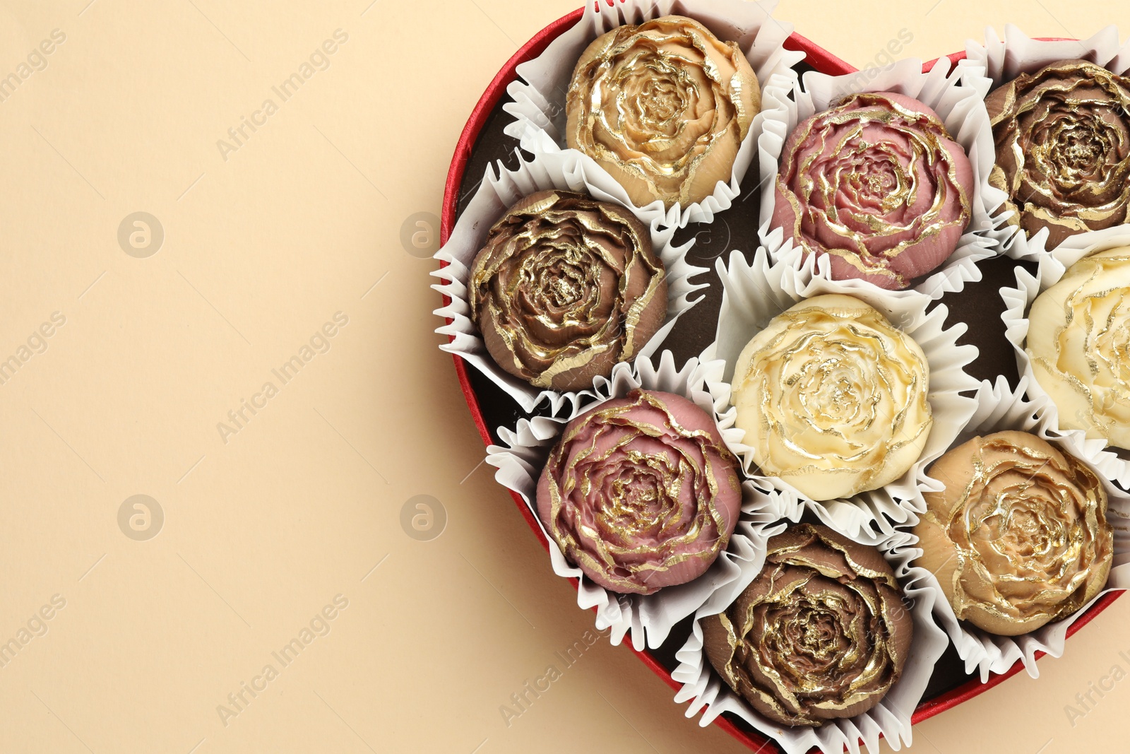 Photo of Flower shaped chocolate bonbons in box on beige background, top view. Space for text