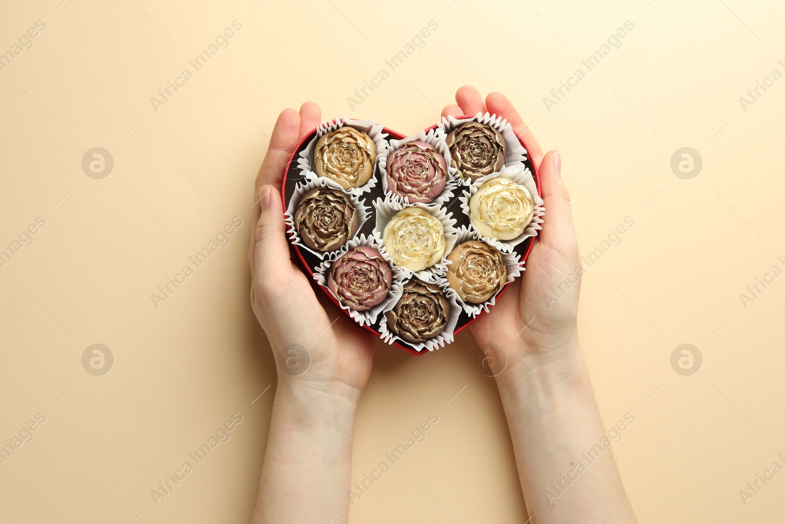 Photo of Woman with box of delicious flower shaped chocolate bonbons on beige background, top view