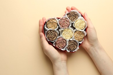 Photo of Woman with box of delicious flower shaped chocolate bonbons on beige background, top view. Space for text