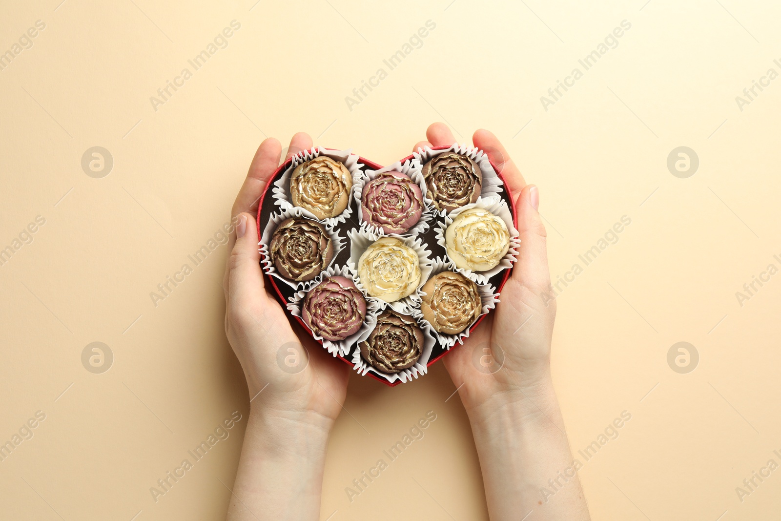 Photo of Woman with box of delicious flower shaped chocolate bonbons on beige background, top view