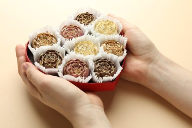 Photo of Woman with box of delicious flower shaped chocolate bonbons on beige background, closeup