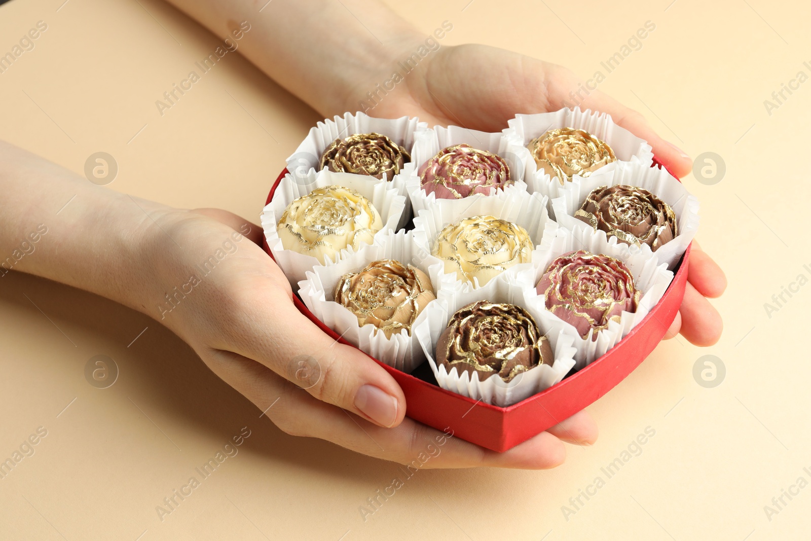 Photo of Woman with box of delicious flower shaped chocolate bonbons on beige background, closeup