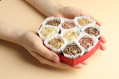 Photo of Woman with box of delicious flower shaped chocolate bonbons on beige background, closeup