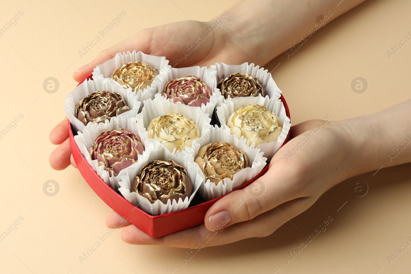 Photo of Woman with box of delicious flower shaped chocolate bonbons on beige background, closeup