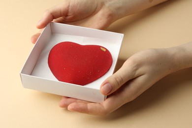 Photo of Woman with heart shaped chocolate in box on beige background, closeup