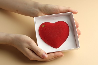 Photo of Woman with heart shaped chocolate in box on beige background, closeup