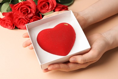 Photo of Woman with heart shaped chocolate and roses on beige background, closeup