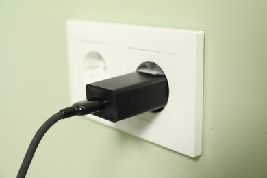 Photo of USB adapter with cable plugged into electric socket on light green wall, closeup