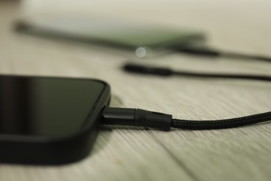 Photo of USB charge cable connected to smartphone on wooden table, closeup