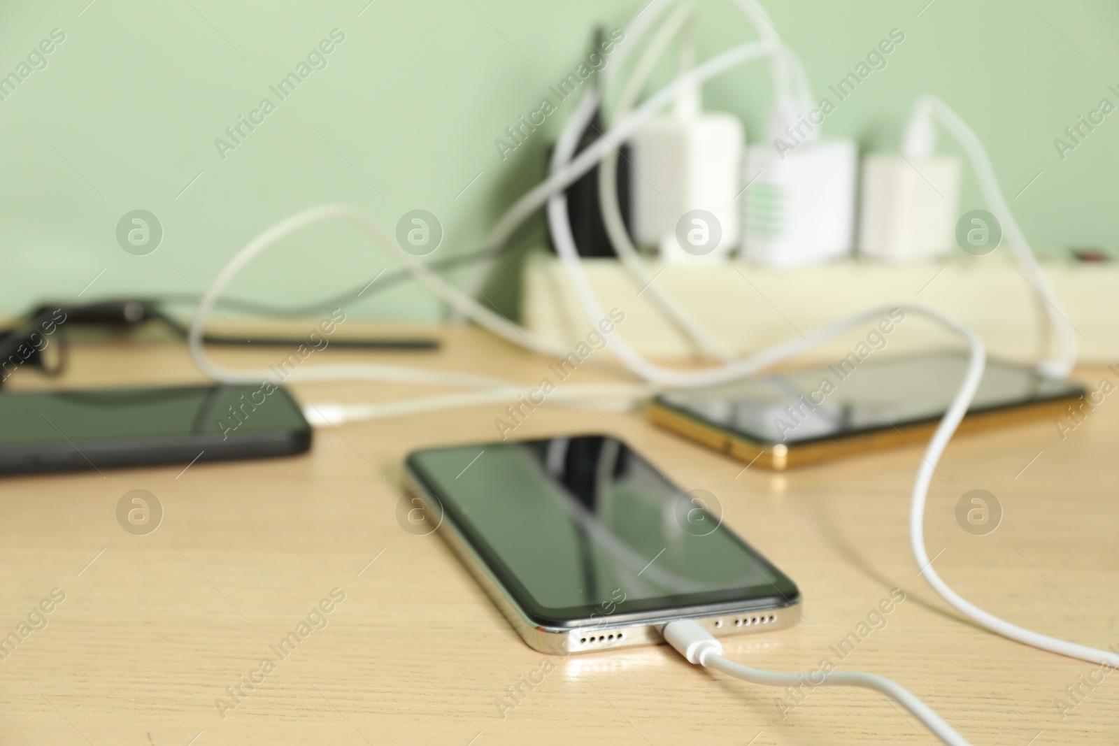 Photo of USB adapters with cables plugged into power strip charging devices on wooden table, closeup